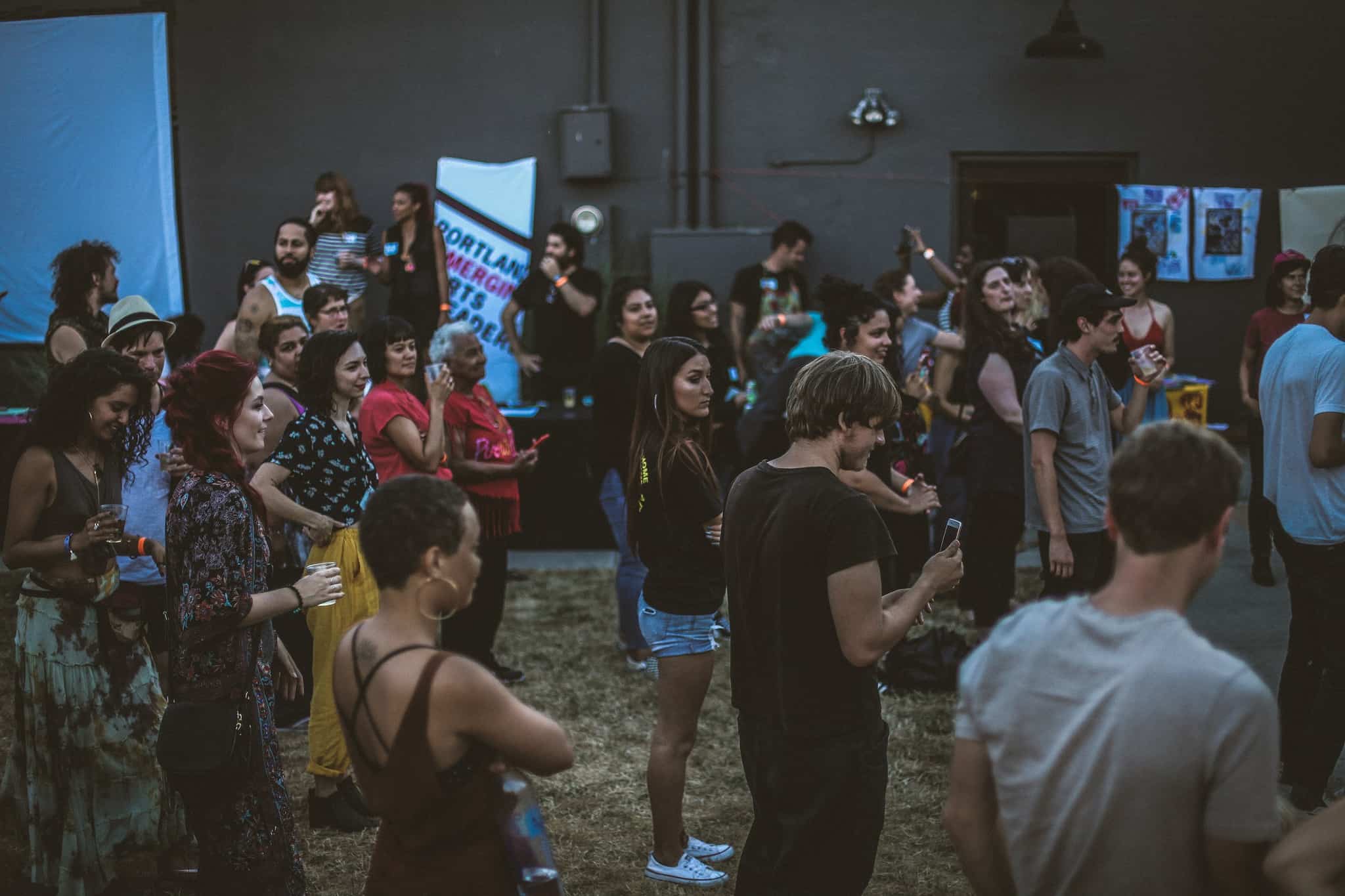 Art Spark attendees stand on the grass facing the stage, listening to a speaker