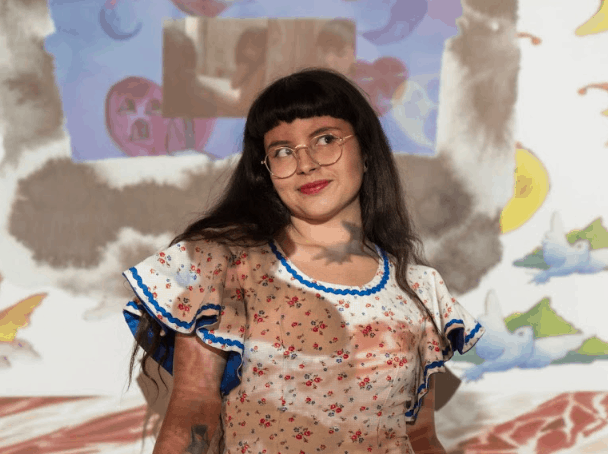 Photo of artist Laura Medina standing in front of a wall, with her artwork projected onto her and the wall.