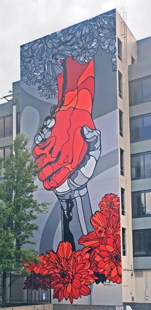 Image of a large building mural with two hands clasped, one red and one grey, emerging from the flowers.